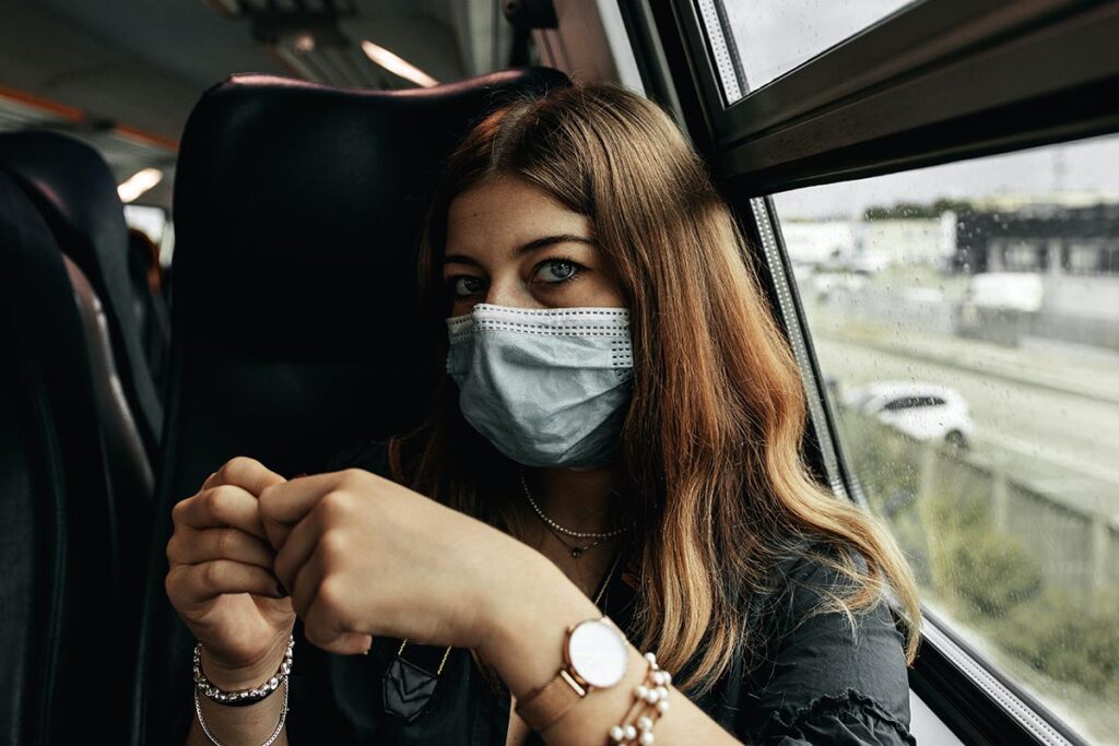 Eine Frau sitzt mit OP-Maske im Zug.