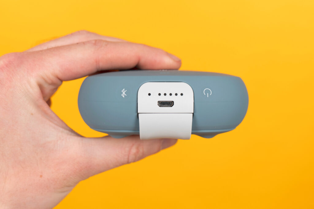 Hand hält hellblaue Bluetooth-Box zwischen Fingern von Seite vor gelben Hintergrund