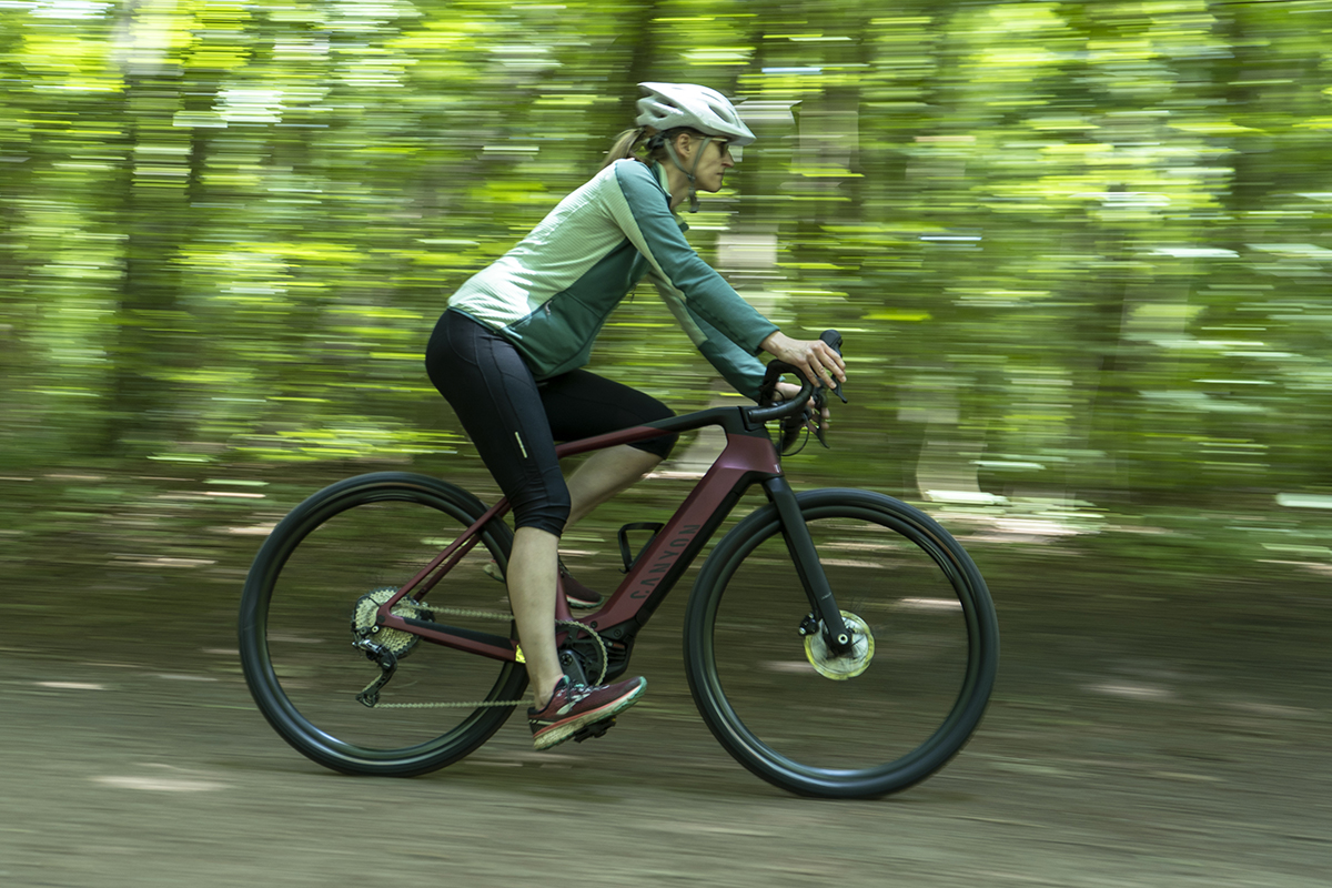 Frau fährt auf E-Gravel-Bike durch einen Wald