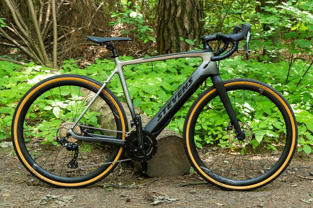 Seitenansicht: E-Gravel-Bike von Stevens lehnt an einem Baumstamm im Wald.