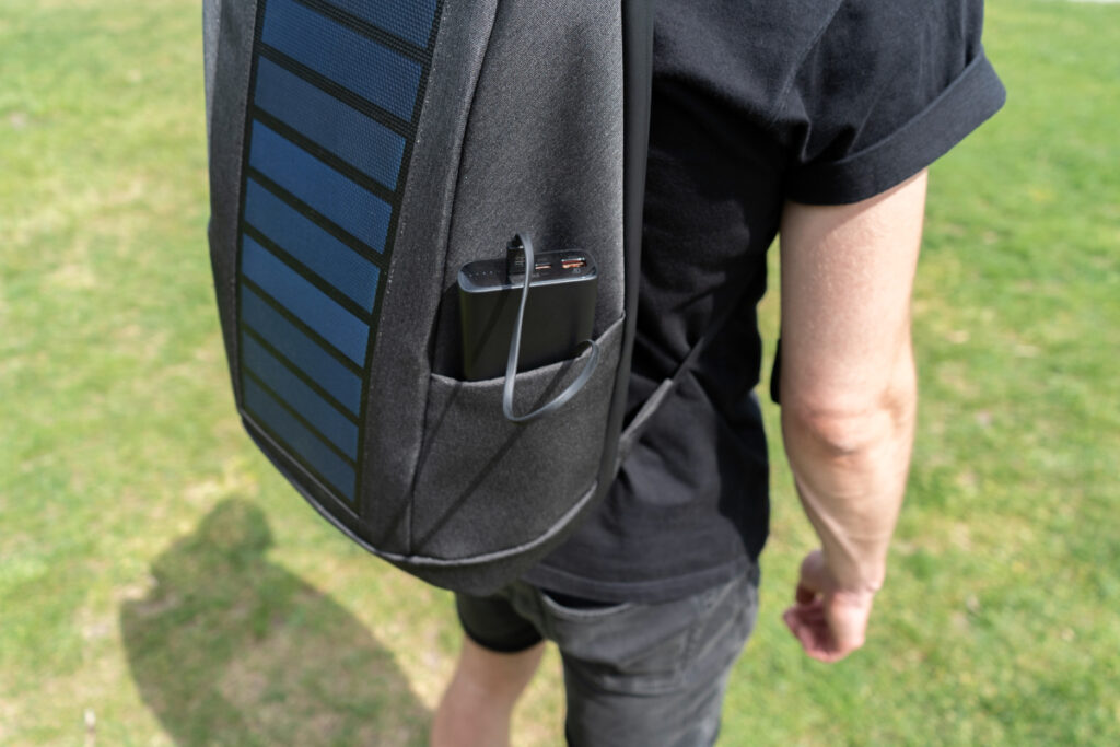Ein getragener Solarrucksack lädt ein Smartphone auf.