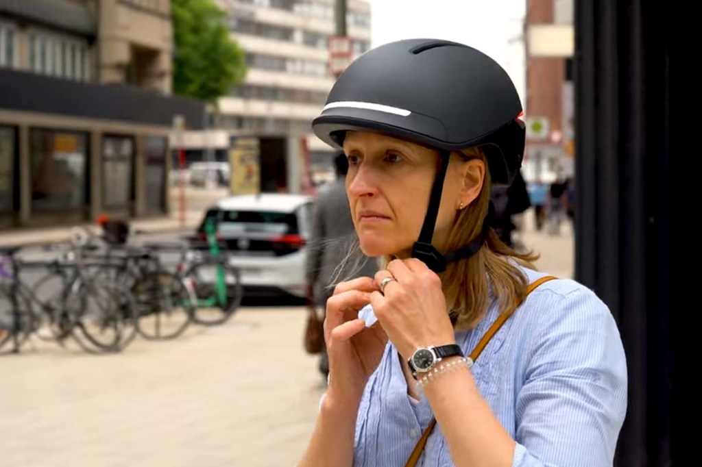 Frau ist gerade dabei, die Lasche eines Fahrradhelms zu schließen, städtischer Hintergrund