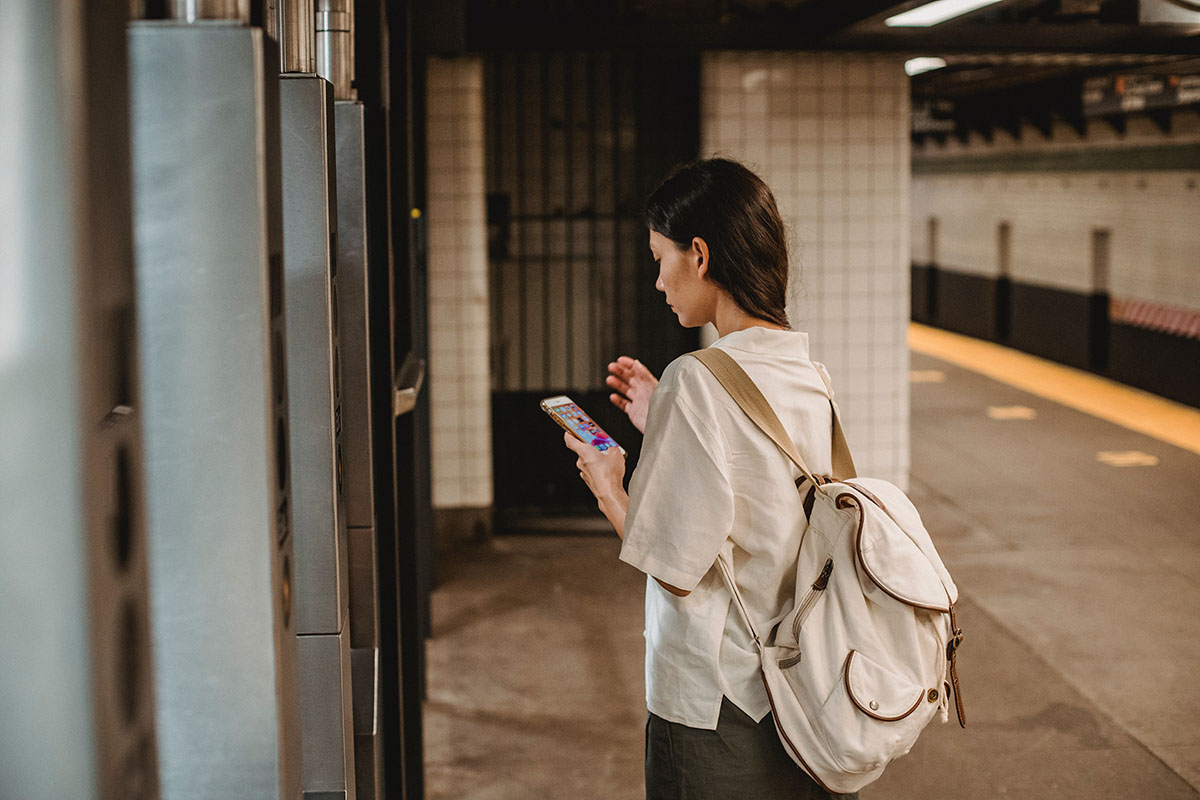 Eine Frau steht an einer Bahnstation und benutzt ein Smartphone.