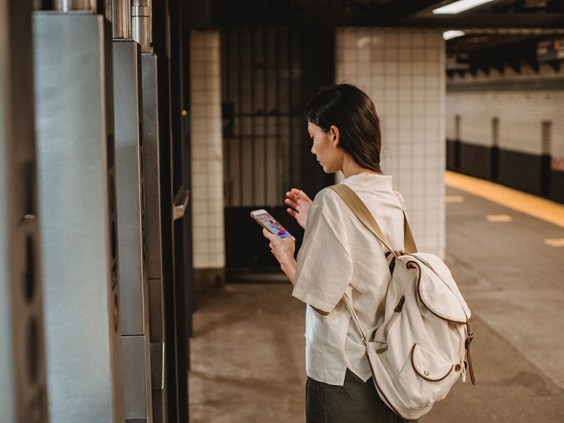 Eine Frau steht an einer Bahnstation und benutzt ein Smartphone.