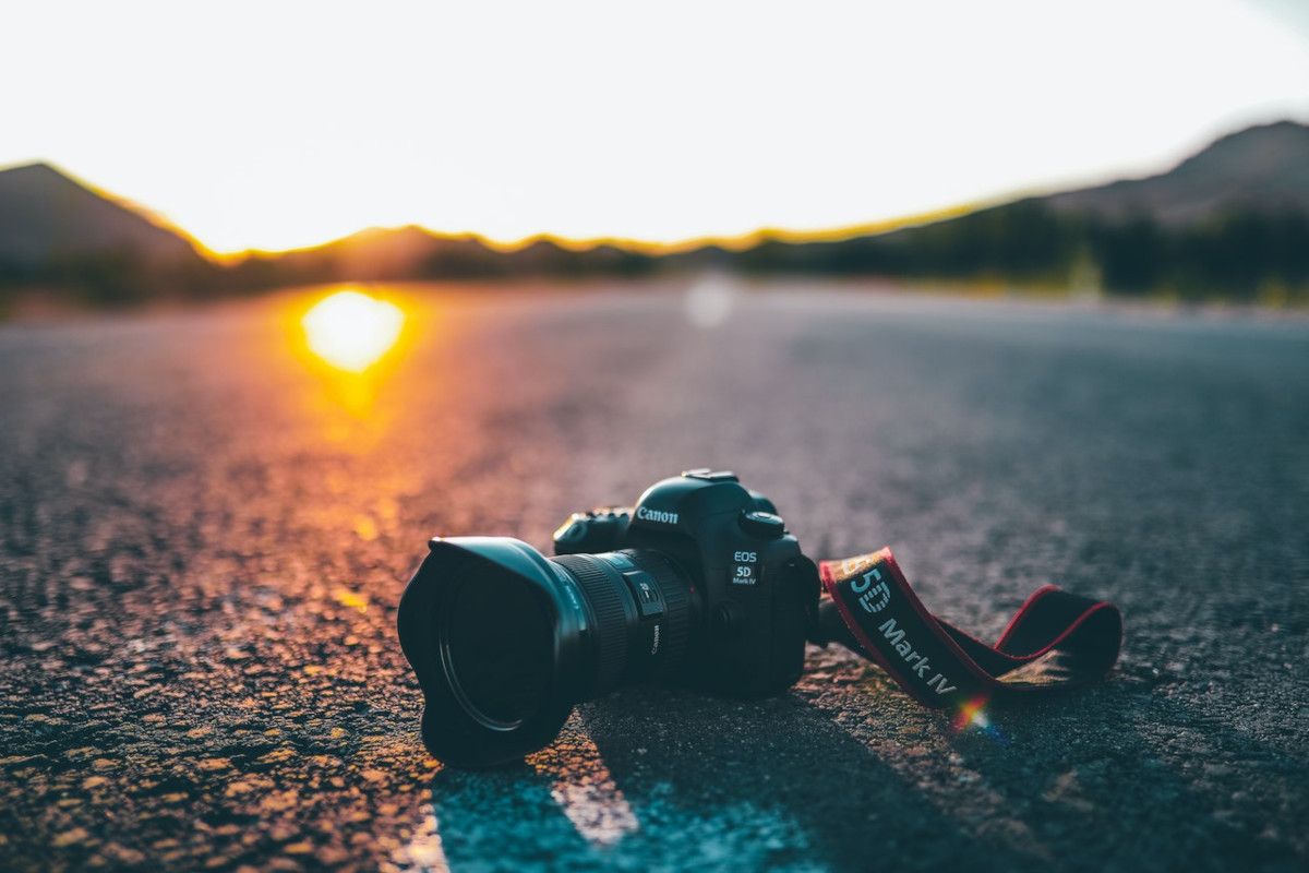 Schwarze Spiegelreflexkamera liegt auf asphaltierter Straße in Landschaft mit Sonnenuntergang