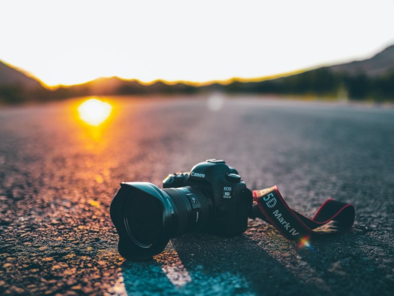 Schwarze Spiegelreflexkamera liegt auf asphaltierter Straße in Landschaft mit Sonnenuntergang