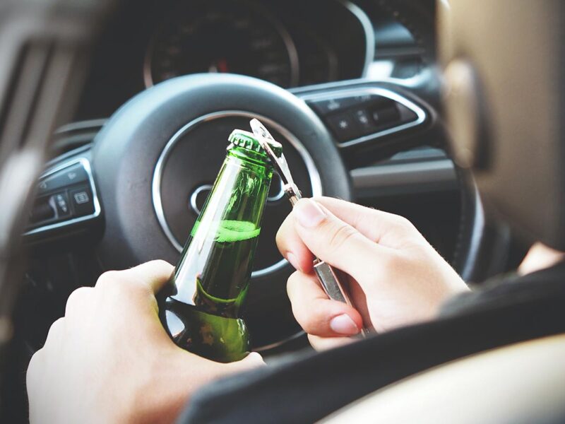 Eine Bierflasche wird am Steuer eines Autos geöffnet.