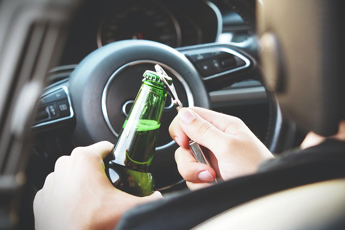 Eine Bierflasche wird am Steuer eines Autos geöffnet.