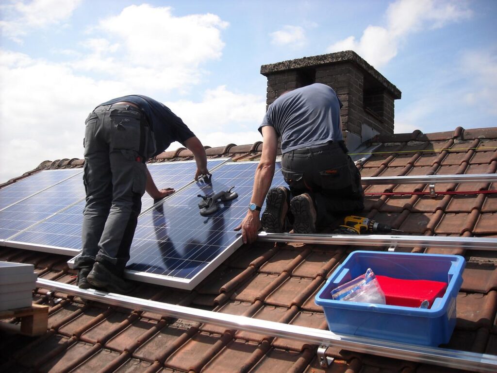 Zwei Männer von hinten bringen auf rotem Dach Solar-Module an