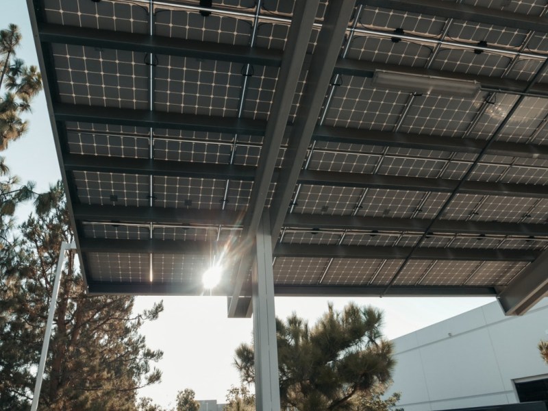 Solarcarport von unten mit Bäumen im Hintergrund und weißem Gebäude