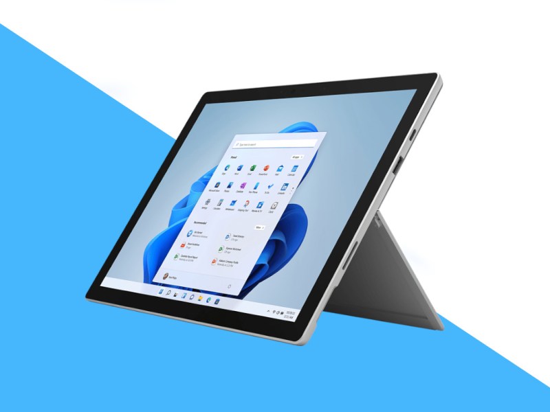 Aufgestelltes silbernes Surface Pro 7 plus Tablet mit Windows 11 Startbildschirm schräg von vorne auf weiß blauem Hintergrund