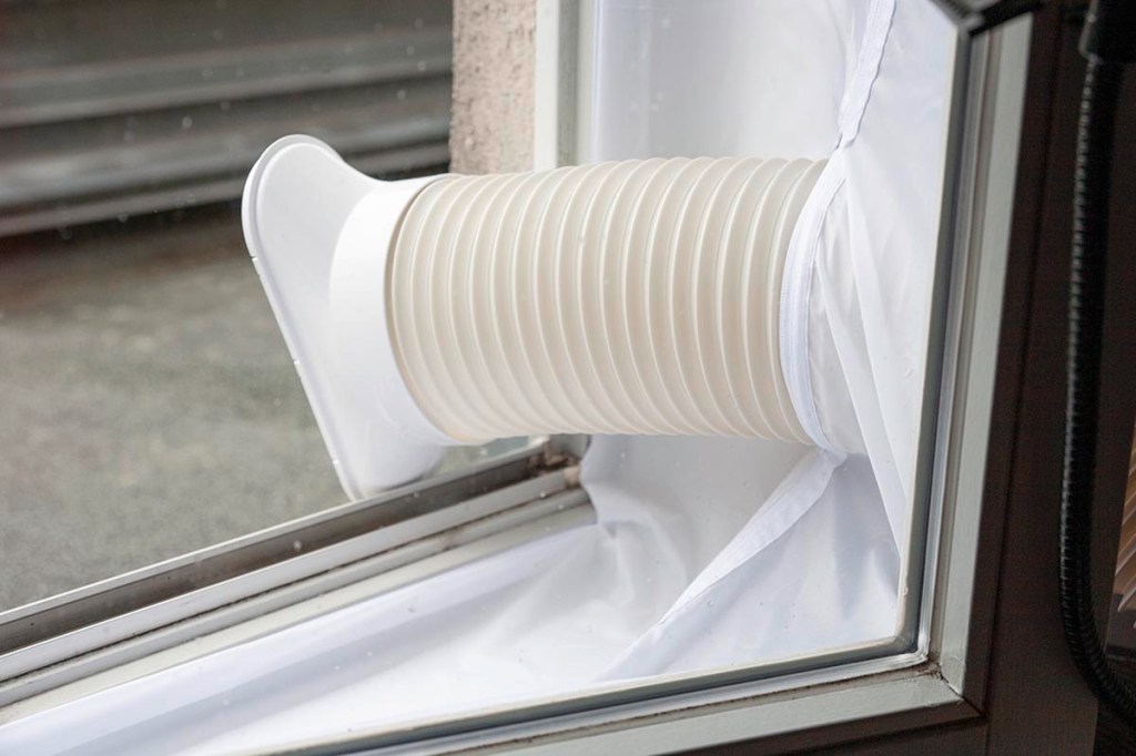 Abluftschlauch in weiß von klimagerät ragt aus geöffnetem Fenster