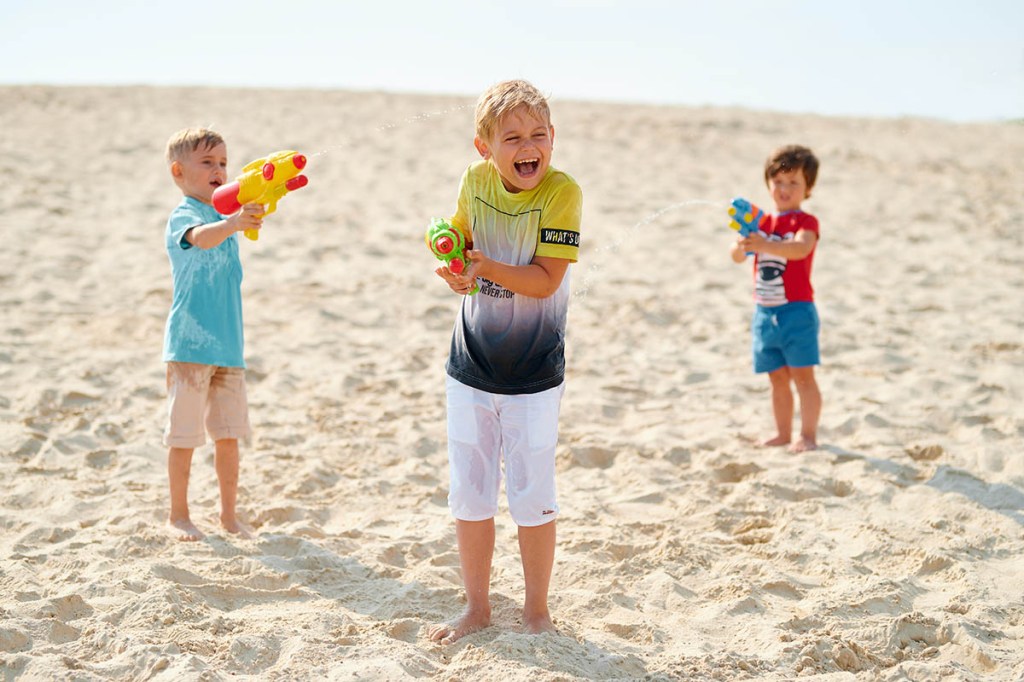 Drei Kinder spielen am Strand mit Wasserpistolen.