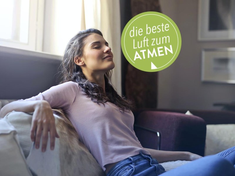 Eine Frau sitzt auf dem Sofa und atmet ein.