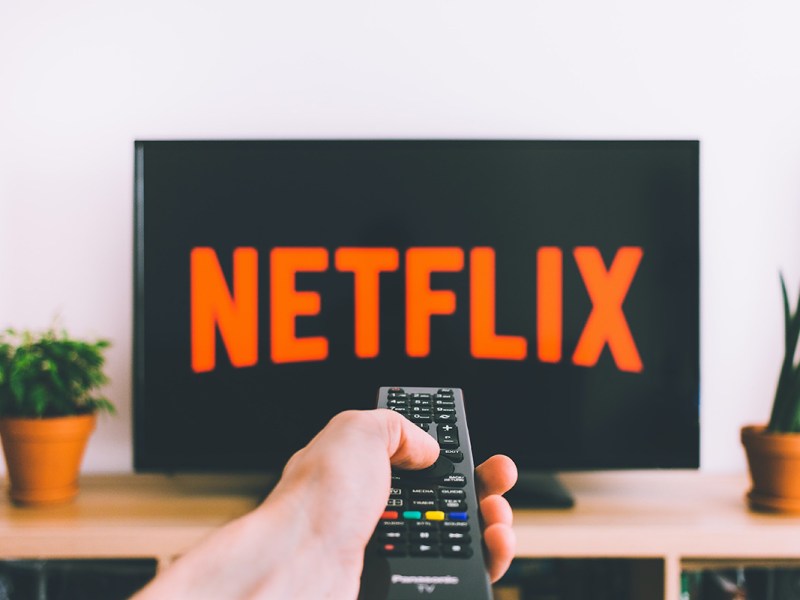 Eine Fernbedienung zeigt auf einen Fernseher, auf dem das Netflix Logo zu sehen ist.
