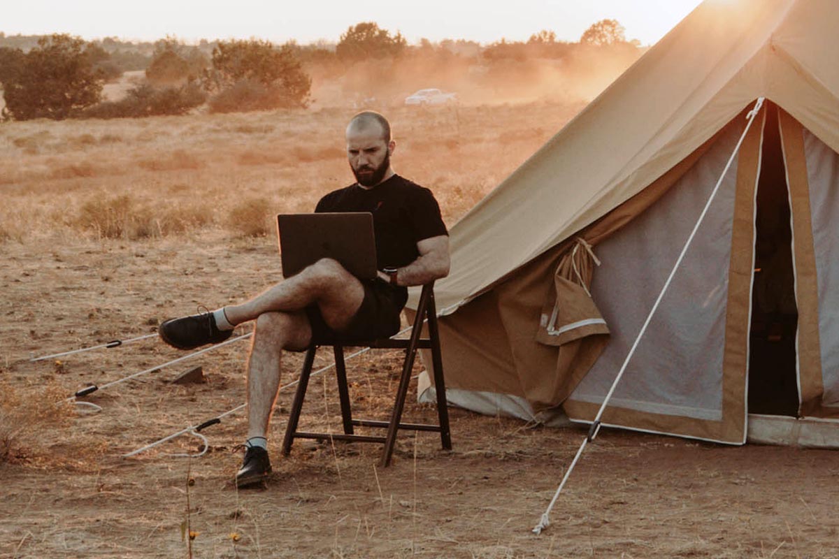 Mann mit Laptop im Urlaub vor seinem Zelt