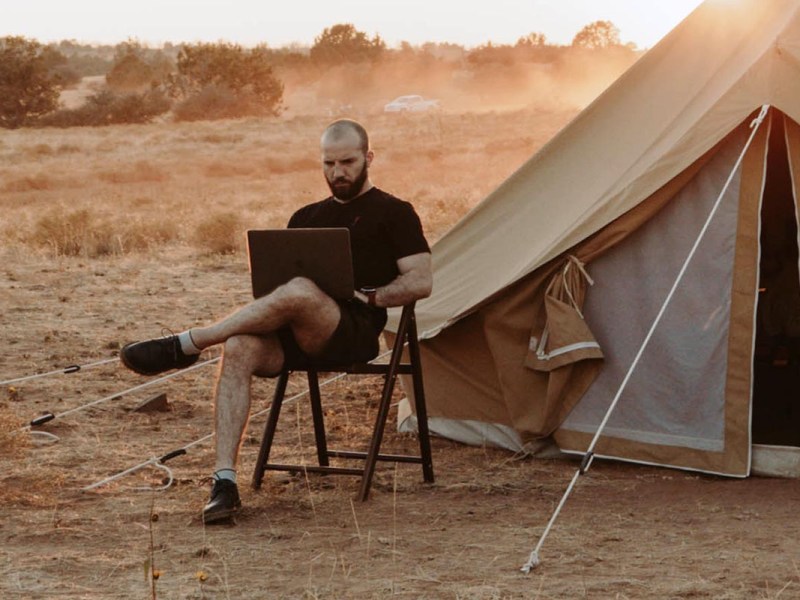 Mann mit Laptop im Urlaub vor seinem Zelt