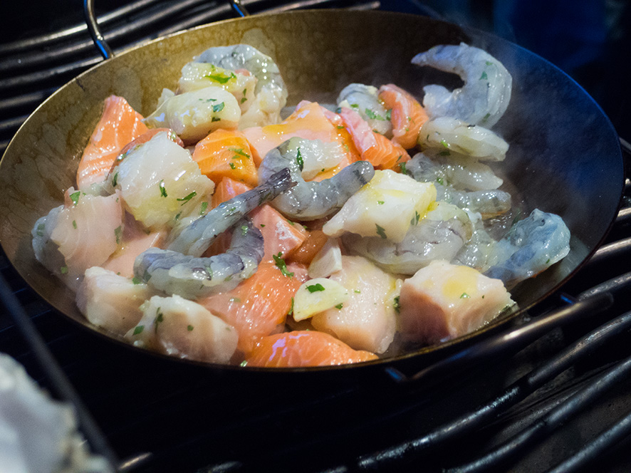 Diverse Fischfiletstücke in einer Pfanne auf einem Grillrost