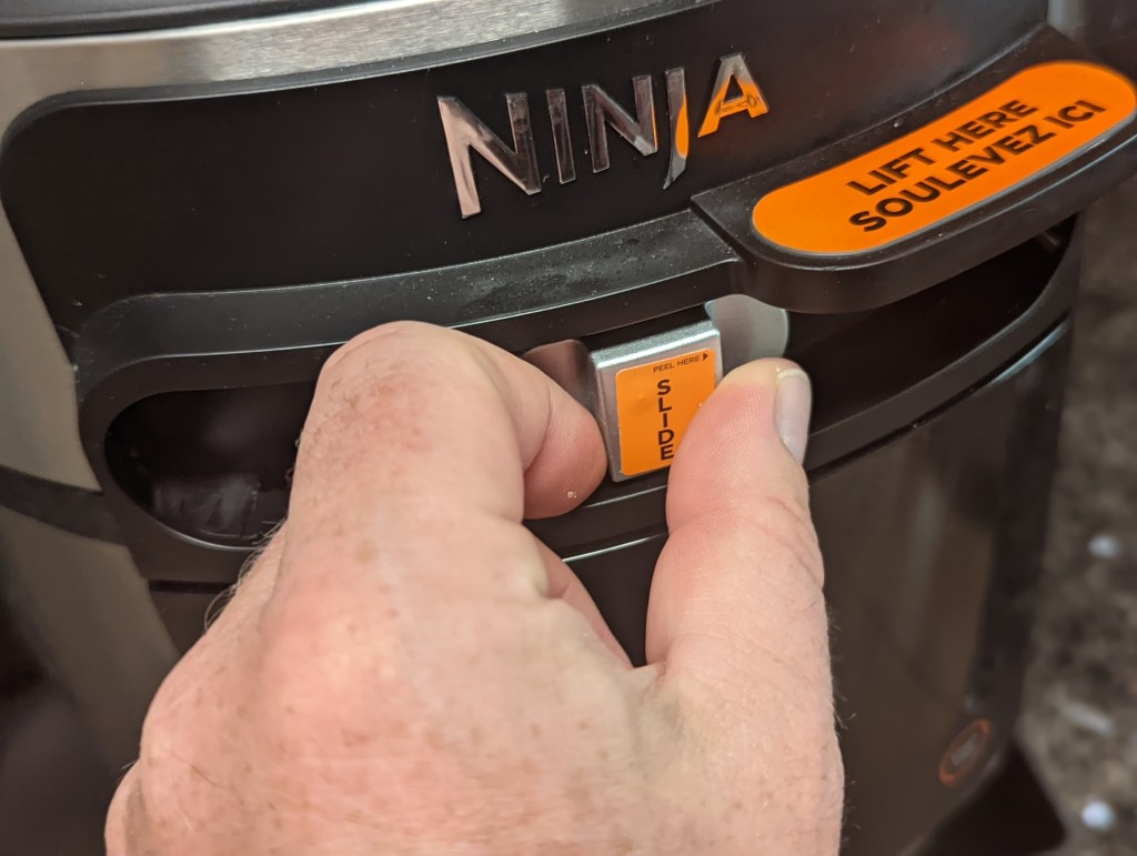 Zwei Finger bewegen den Verriegelungsschieber des Ninja Foodi