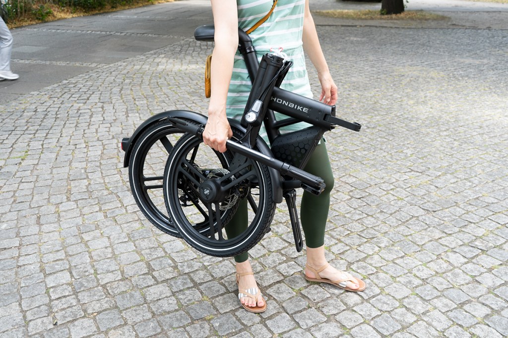E-Faltrad von Honbike, Frau trägt gefaltetes Rad