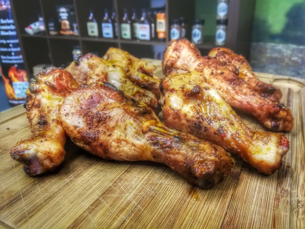 Die 25 besten Grill-Rezepte fürs Camping: Hähnchenunterkeulen (Drumsticks) auf einem Brett vor unscharfem Hintergrund