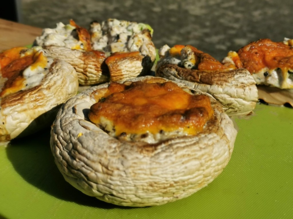 Die 25 besten Grill-Rezepte fürs Camping: Mit Cheddar überbackene Champignons auf einem grünen Brett