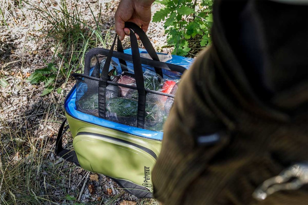 Eine Person trägt die Petromax Kühltasche mit eingesetzter Netztasche und Lebensmitteln.