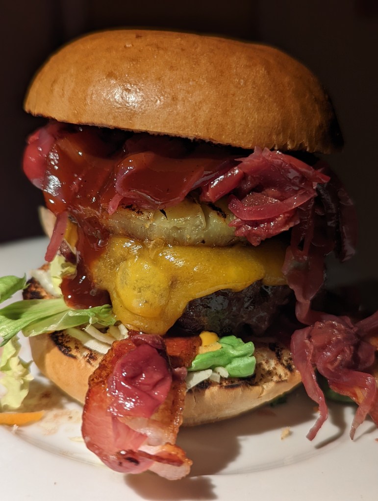 Die 25 besten Grill-Rezepte fürs Camping: Ein großer Burger, belegt mit Bacon, Käse und roten Schmorzwiebeln