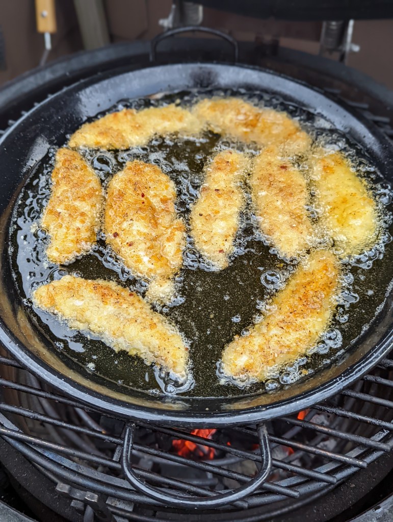 Goldgelbe Hähnchenfilets in Pako-Panade werden in einer Pfanne mit Öl auf dem Grill gebraten