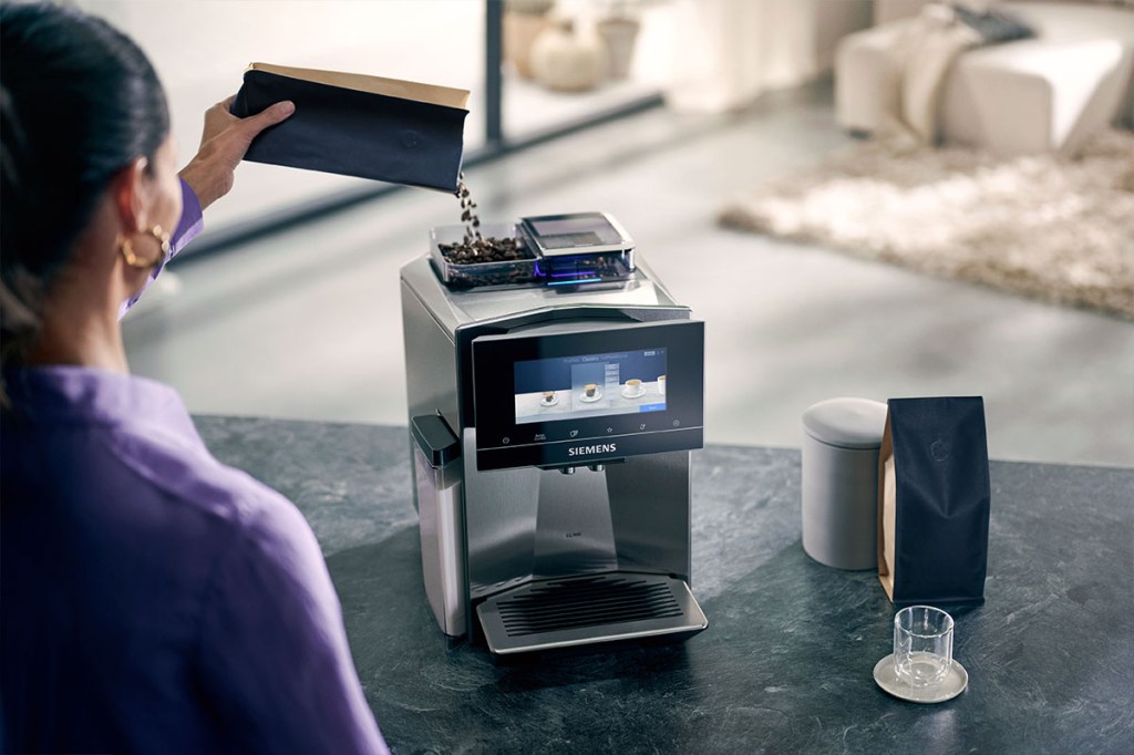 Es ist eine Person zu sehen, die den neuen Siemens EQ900-Kaffeevollautomaten mit Kaffeebohnen befüllt.