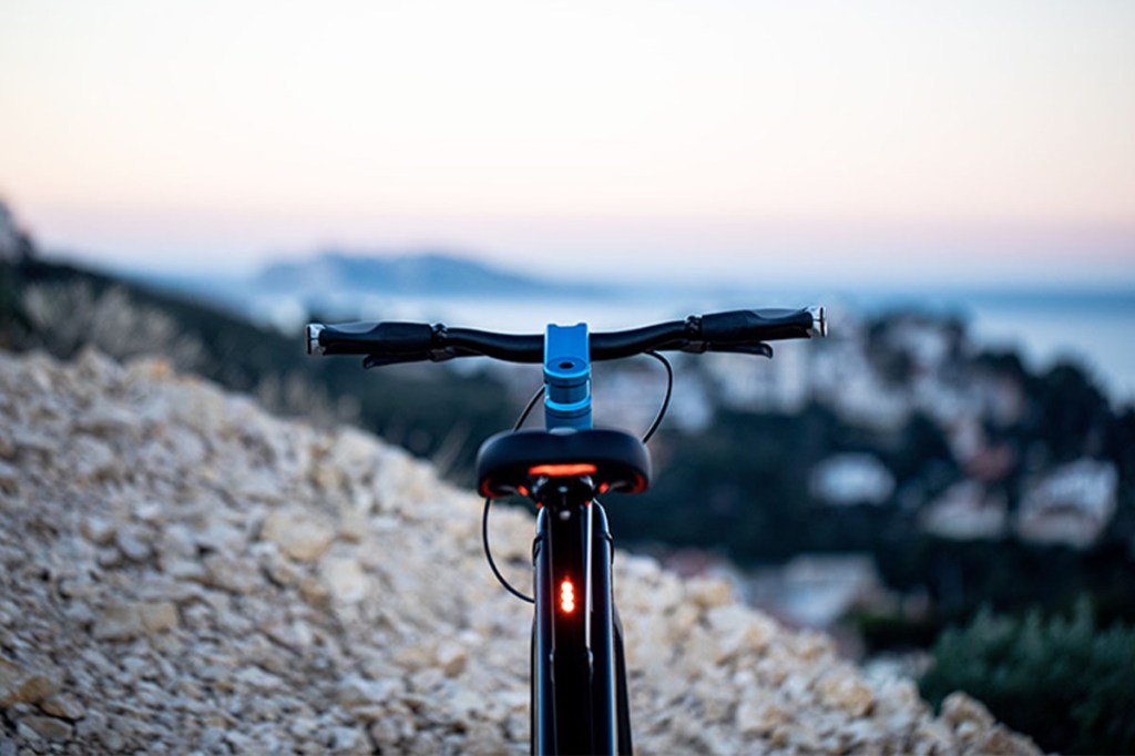 Verschwommenes Landschaftspanorama im Hintergrund, im Vordergrund E-Bike von Iweech von hinten abgebildet
