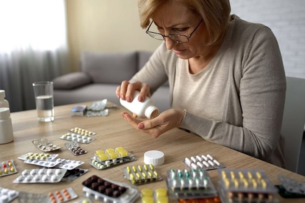 Eine Frau sitzt vor einem Tisch voller verschiedener Tabletten.