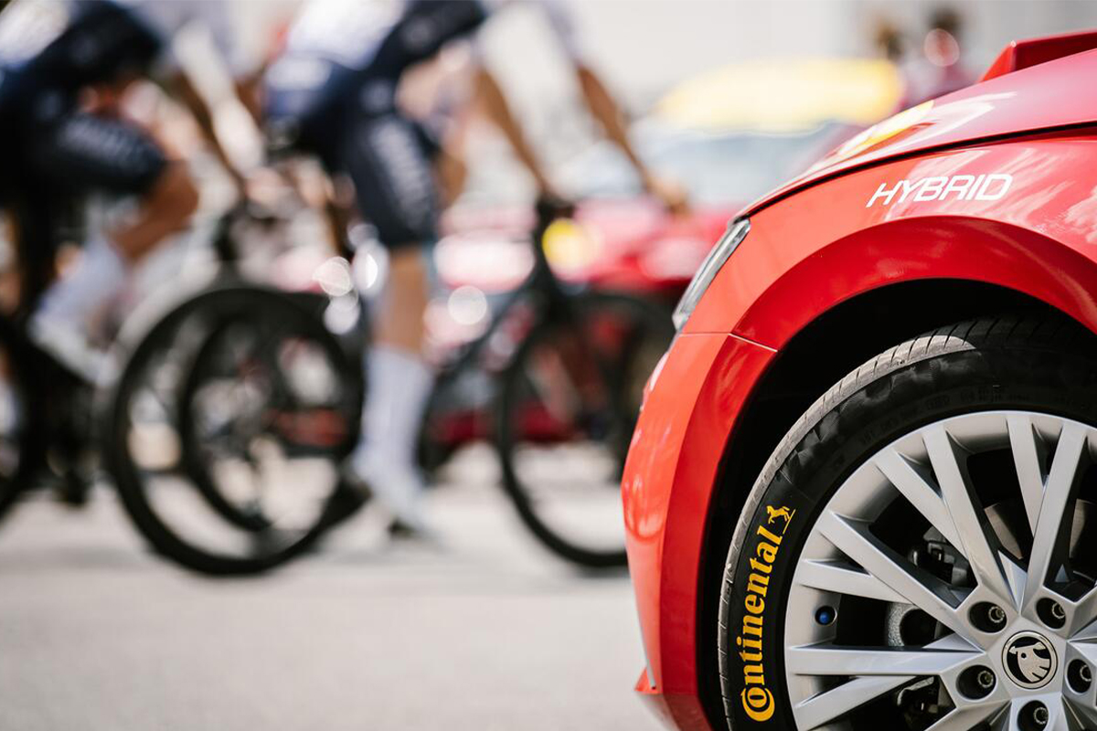Angeschnittenes Auto mit Reifen im Vordergrund, im Hintergrund in der Unschärfe Fahrradfahrer