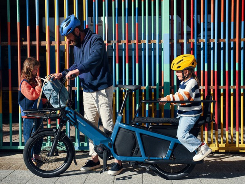 Mann und zwei Kinder mit E-Cargo-Bike Multitinker von Riese & Müller vor Hauswand
