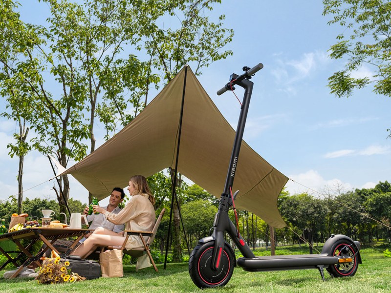 Paar sitzt unter einer Zeltplane im Grünen. Vor Ihnen steht der E-Scooter 4mPro von Xiaomi.
