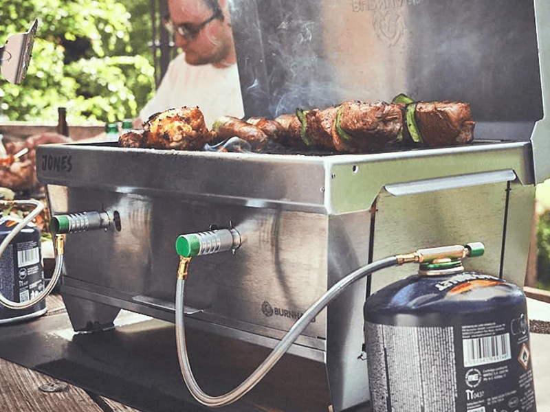 Der Burnhard Jones auf einem Holztisch in Aktion. Auf dem Rost liegt Grillgut.