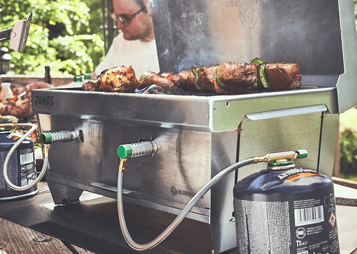 Der Burnhard Jones auf einem Holztisch in Aktion. Auf dem Rost liegt Grillgut.