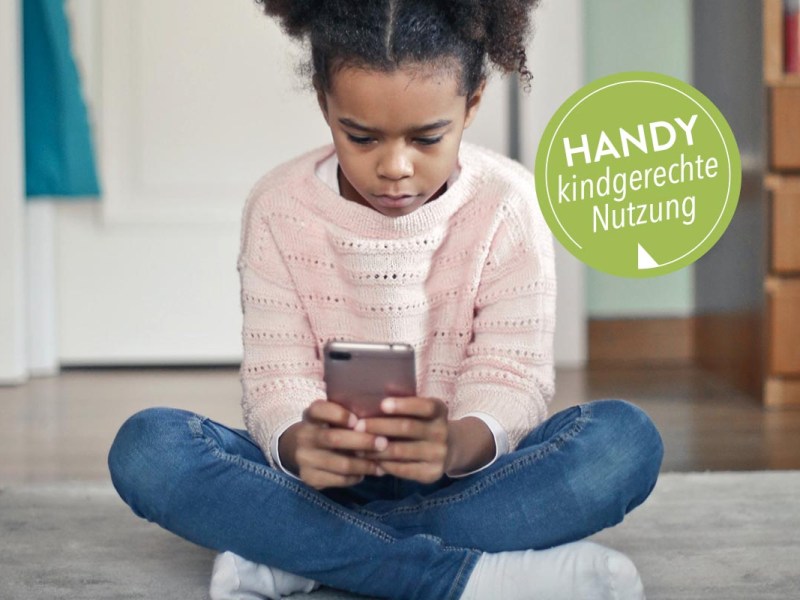 Ein Kind mit Smartphone in der Hand auf dem Boden sitzend.