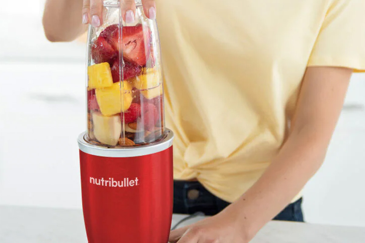 Eine Person macht sich einen Smoothie aus bunten Früchten im roten Nutribullet Pro 900 Smoothiemaker.