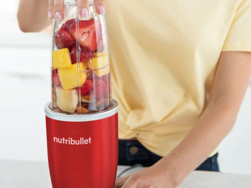 Eine Person macht sich einen Smoothie aus bunten Früchten im roten Nutribullet Pro 900 Smoothiemaker.