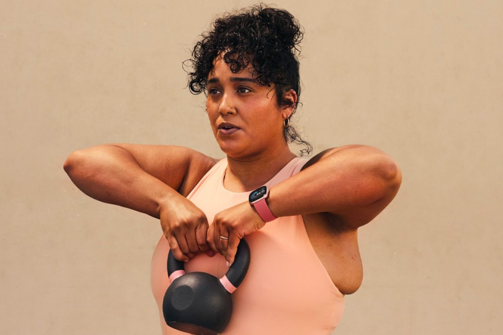 Eine Frau macht mit der Fitbit Versa 4 am Arm Gewichtheben.