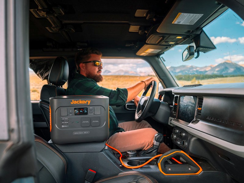 Mann fährt im Auto durch Wüstenlandschaft. Auf dem Beifahrersitz steht ein Jackery Explorer 1000 Pro Solargenerator.