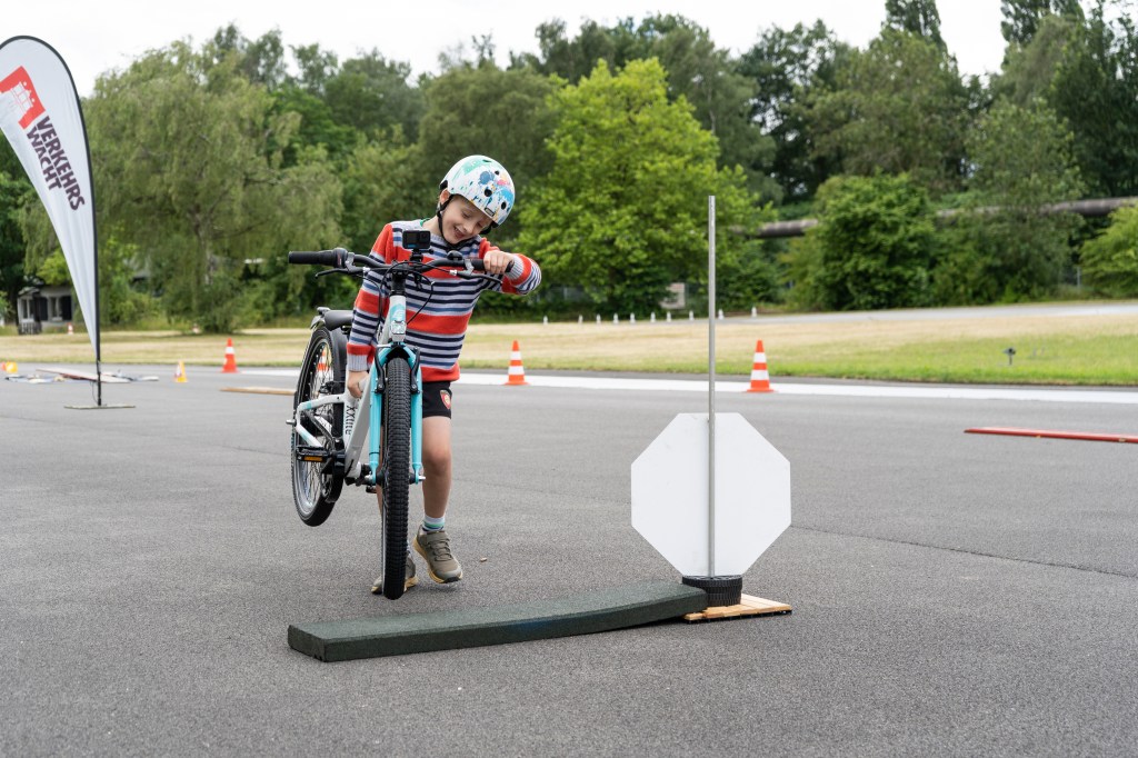 Kind trägt ein Fahrrad über ein Hindernis