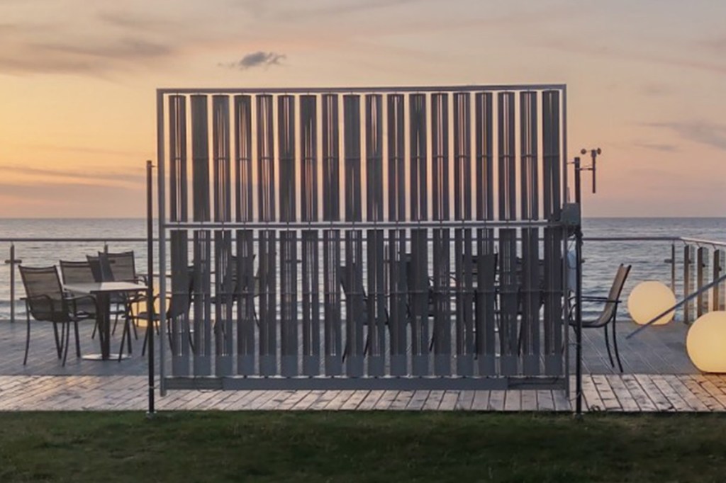 Der Windkraft-Zaun ist vor einer Terrasse am Meer gezeigt.