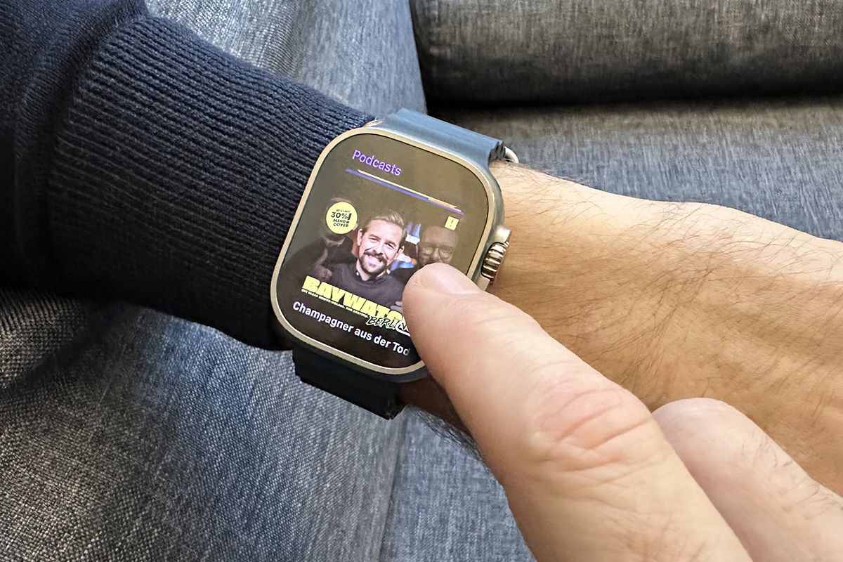 Smartwatch an Männerarm mit blauem Pulli zeigt Podcast Folge