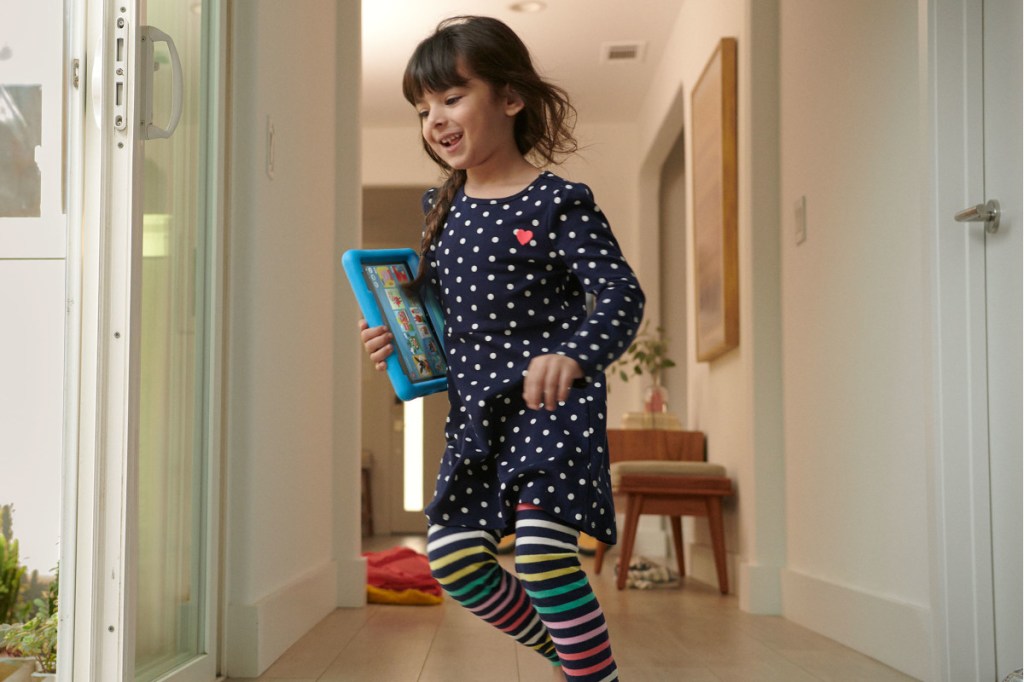 Mädchen rennt mit blauem Fire HD 8 Kids Tablet im Arm durch Hausflur