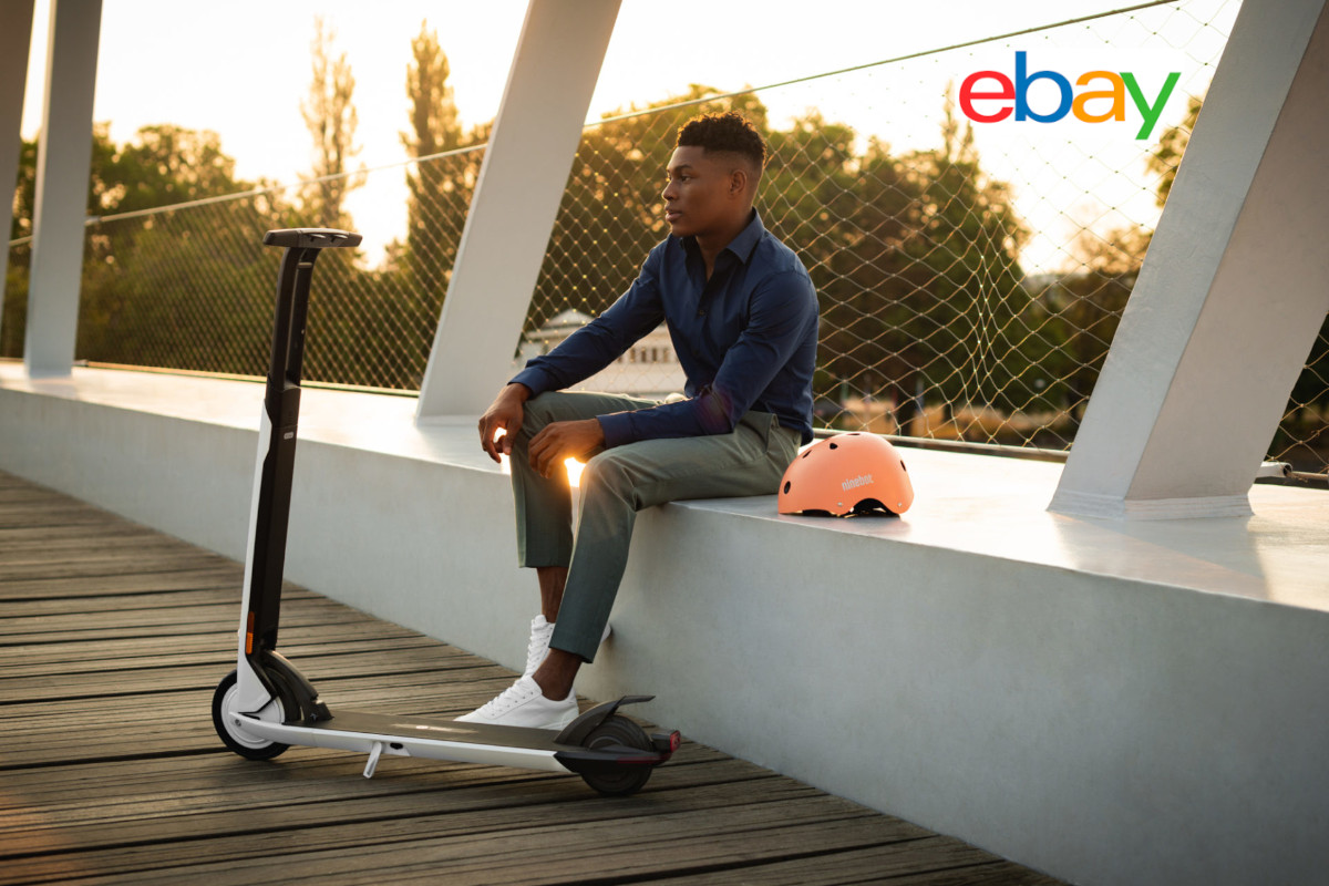 Junger Mann sitzt auf weißém Brückengeländer, davor weißer E-scooter, eBay logo rechts oben