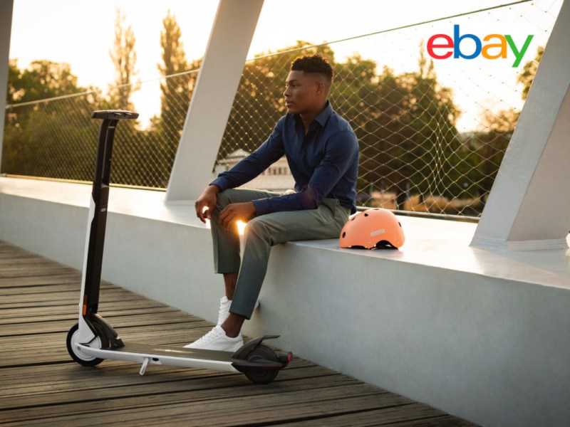 Junger Mann sitzt auf weißém Brückengeländer, davor weißer E-scooter, eBay logo rechts oben