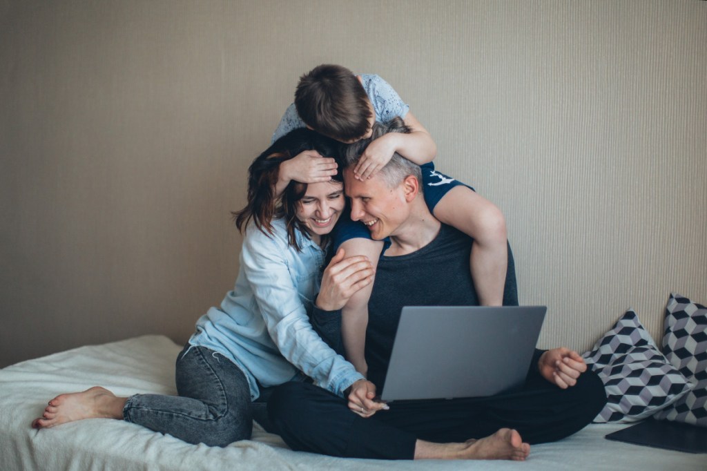 Eltern und Kind sitzen auf Bett mit Laptop und surfen mit o2 Internet.