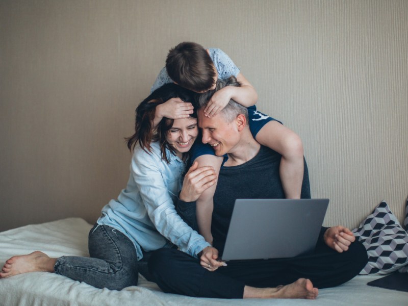 Eltern und Kind sitzen auf Bett mit Laptop und surfen mit o2 Internet.